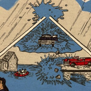 May include: A light blue t-shirt with a comic book style illustration depicting a flood scene. The image includes a house, cars, and people in a raft, with water splashing around.