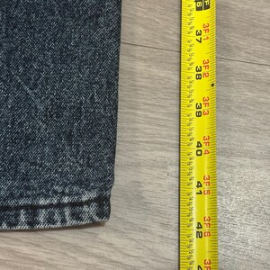 May include: Close-up of dark blue denim fabric with a yellow measuring tape. The tape shows measurements from 37 to 42 inches. The denim has a textured appearance.