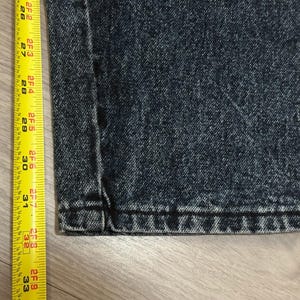 May include: Close-up of dark wash denim jeans with a yellow measuring tape. The tape shows measurements from 26 to 33 inches. The jeans have a classic five-pocket design.