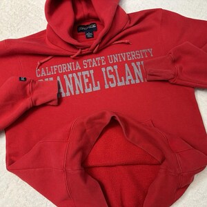Puede incluir: Sudadera roja con capucha con el texto "California State University Channel Islands" en letras grises.