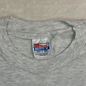 May include: Close-up of a heather gray Hanes Beefy-T adult XL t-shirt. The tag is visible, showing the brand logo and size information. The shirt is made of a soft, comfortable material.