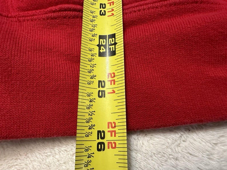 Puede incluir: Primer plano de una tela roja medida con una cinta m&eacute;trica amarilla. La cinta m&eacute;trica muestra 2 pies 6 pulgadas.