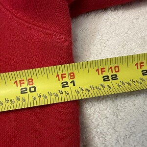 Puede incluir: Una cinta m&eacute;trica amarilla con marcas negras se coloca sobre una superficie de tela roja. La cinta mide hasta 58,4 cm.