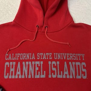 Puede incluir: Sudadera roja con capucha con el texto "CALIFORNIA STATE UNIVERSITY CHANNEL ISLANDS" en letras grises.