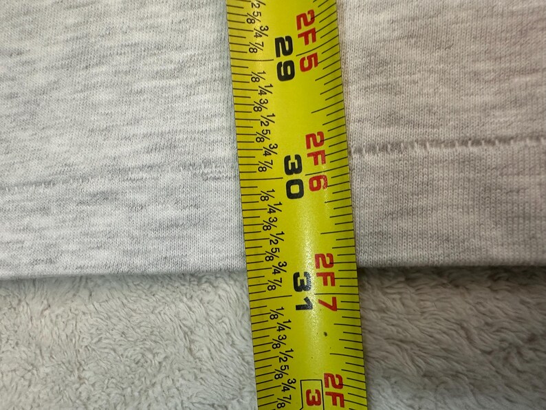 May include: A close-up shot of a gray fabric with a yellow and black measuring tape. The tape shows measurements in inches, with the numbers 29, 30, and 31 clearly visible. The fabric has a textured appearance.