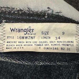 May include: Close-up of a Wrangler brand tag on denim jeans. The tag indicates size 9, length 34 inches, and style 16MWZNF. It also includes washing instructions and states "Made in USA."