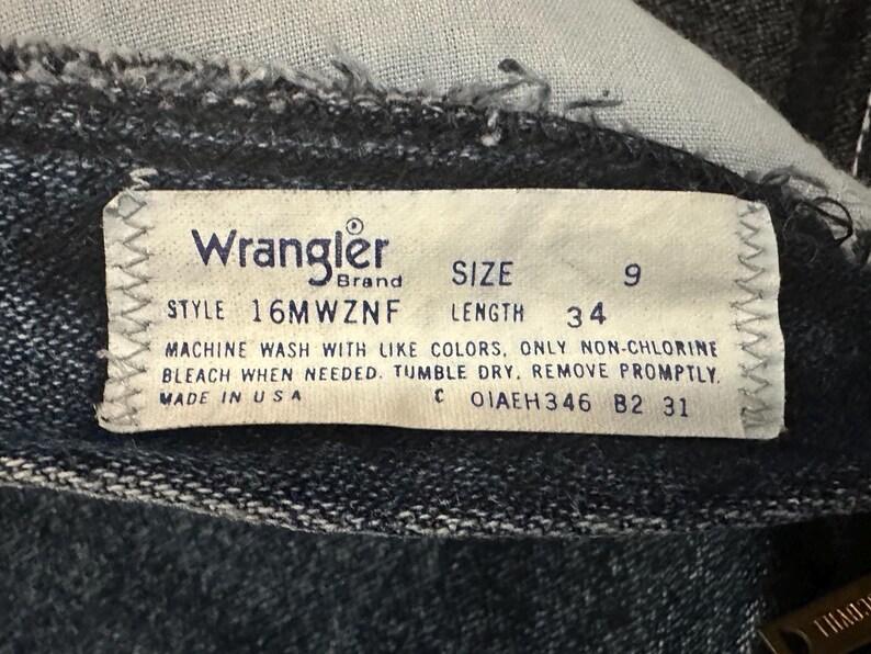 May include: Close-up of a Wrangler brand tag on denim jeans. The tag indicates size 9, length 34 inches, and style 16MWZNF. It also includes washing instructions and states "Made in USA."