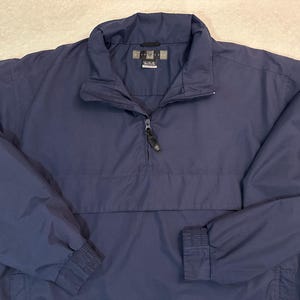 May include: Navy blue pullover jacket with a quarter-zip and a small white Nike logo on the sleeve. The jacket has a stand-up collar and elastic cuffs. The jacket is made of a lightweight, water-resistant material.