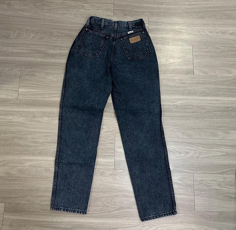 May include: Dark wash denim jeans with a high waist and a classic five-pocket design. The jeans feature a leather patch on the back pocket and a button and zipper closure. The jeans are a size 30 inch waist.