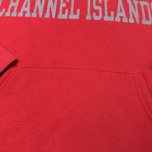 Puede incluir: Sudadera roja con capucha con un logotipo gris "CHANNEL ISLANDS" impreso en la parte delantera.
