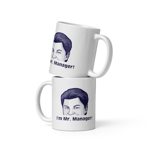 Peut inclure: Deux tasses en céramique blanche empilées l'une sur l'autre. La tasse du haut présente une illustration de dessin animé d'un visage d'homme avec le texte "Mr. Manager!" La tasse du bas présente une illustration de dessin animé d'un visage d'homme avec le texte "I'm Mr. Manager!"