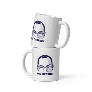 May include: Two white ceramic mugs stacked on top of each other. Each mug features a cartoon illustration of a man with glasses and the text "Hey brother".