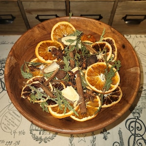 May include: A wooden bowl filled with dried orange slices, cinnamon sticks, star anise, and other spices. The bowl is on a table with a white and black patterned tablecloth.