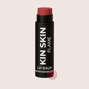 May include: A black lip balm tube with the text "KIN SKIN FLAME" in white. The lip balm itself is a reddish-pink color. The bottom of the tube has the text "LIP BALM" and the website address. A small heart-shaped logo is also visible.