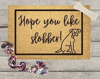May include: A brown doormat with the text "Hope you like slobber!" and a black and white illustration of a dog.