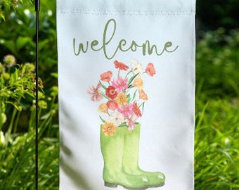 May include: A green garden flag with the word "welcome" in cursive script. The flag features a watercolor illustration of a bouquet of flowers in a pair of green rain boots.