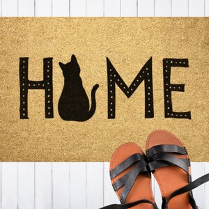 May include: A brown doormat with the word "HOME" in black lettering with a black silhouette of a cat sitting in the middle of the word.