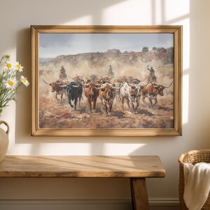 a painting of a group of cattle being herded by a cowboy, displayed on a wall above a wooden table.