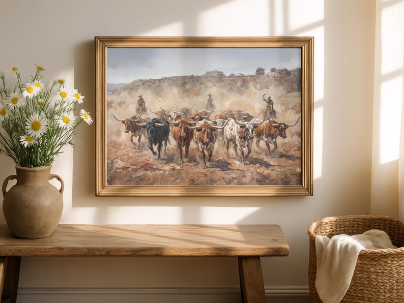 a painting of a group of cattle being herded by a cowboy, displayed on a wall above a wooden table.