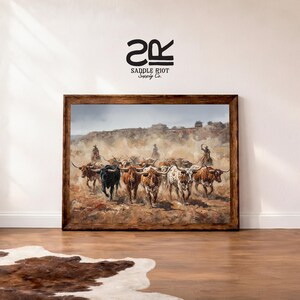 a framed painting of a group of cattle on a dirt road, with a cowboy on horseback leading the herd.