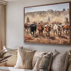 a large painting of a herd of cattle, with a cowboy on horseback leading the animals. The painting is hung on a wall above a couch with decorative pillows.