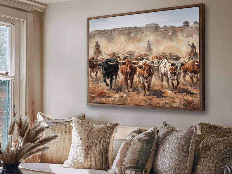 a large painting of a herd of cattle, with a cowboy on horseback leading the animals. The painting is hung on a wall above a couch with decorative pillows.