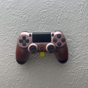 May include: A rose gold PlayStation 4 controller with black buttons and a black touchpad.