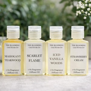 May include: Four small, clear bottles of fragrance diffuser oil with white labels and flip-top caps. The labels read "The Blooming Cactus & Co" and list scents: Mahogany Teakwood, Scarlet Flame, Iced Vanilla Woods, and Strawberry Cream. Each bottle contains 1 fluid ounce.