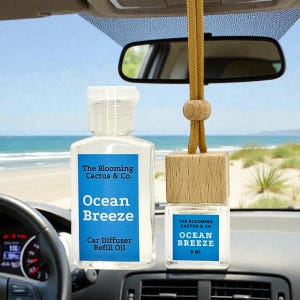 May include: Two car air fresheners and refill oil bottles. The bottles and the refill oil bottle have a blue label with the text "The Blooming Cactus & Co. Ocean Breeze". The air freshener is a wooden block with a hanging cord.