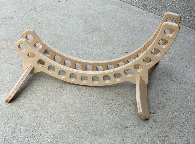 May include: A wooden stand with a curved shape and a series of holes. The stand is made of light wood and has a natural finish.