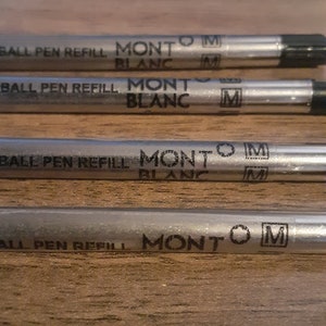 May include: Four silver ballpoint pen refills with black ink. Each refill has the text "BALL PEN REFILL MONT BLANC M" printed on it.