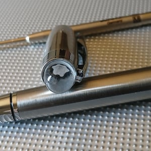 Puede incluir: Dos bolígrafos plateados, uno con un capuchón transparente y el otro con un capuchón negro. El bolígrafo con el capuchón transparente tiene un logotipo Montblanc plateado en el capuchón.