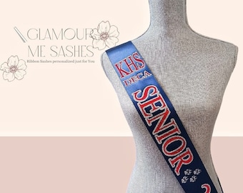May include: A navy blue sash with red glitter lettering that reads "KHS DECA SENIOR 2023" and paw prints.