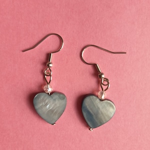 Puede incluir: Un par de pendientes de plata en forma de corazón con una cuenta de cristal transparente en cada pendiente.
