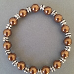 Op de afbeelding: Een bruine kralen armband met zilveren accenten. De armband is gemaakt van ronde kralen en heeft een eenvoudig ontwerp.