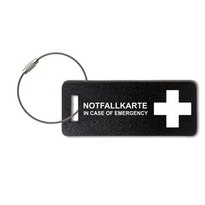 May include: Black rectangular tag with a white cross and the text "NOTFALLKARTE IN CASE OF EMERGENCY". The tag is attached to a silver key ring.