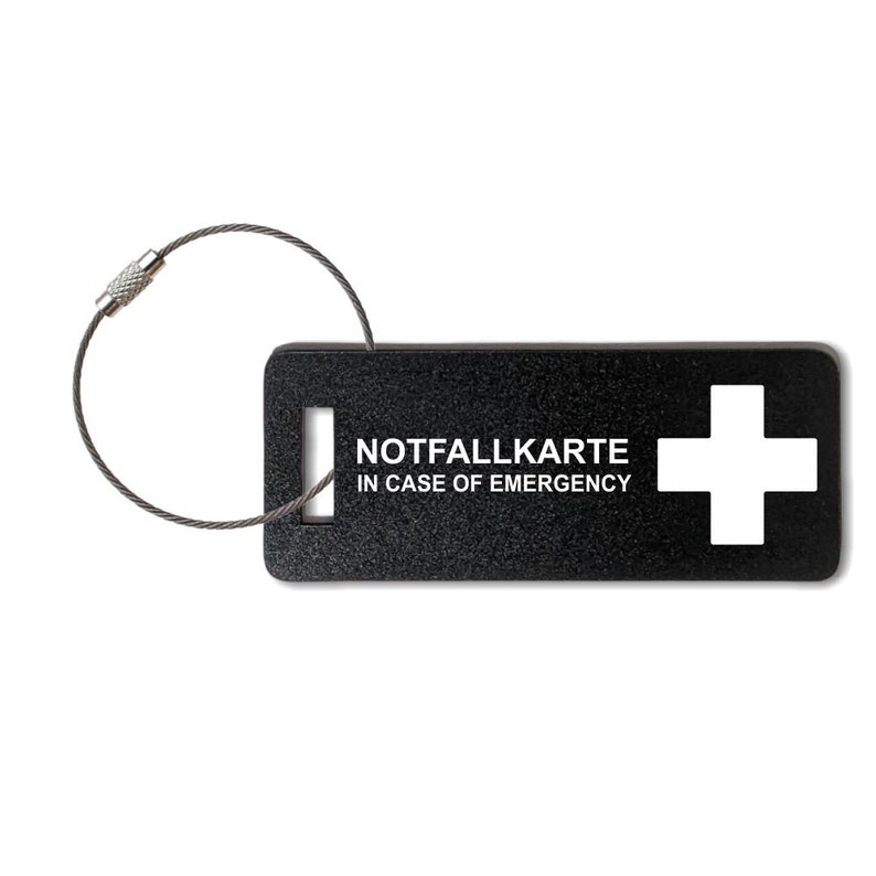 May include: Black rectangular tag with a white cross and the text "NOTFALLKARTE IN CASE OF EMERGENCY". The tag is attached to a silver key ring.