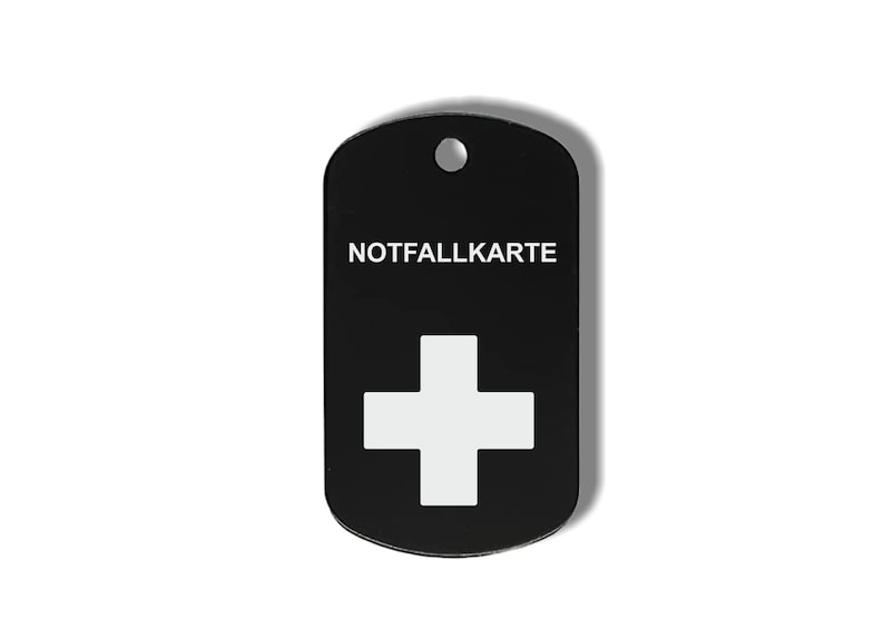 May include: Black metal dog tag with a white Swiss cross and the text "NOTFALLKARTE" in white.
