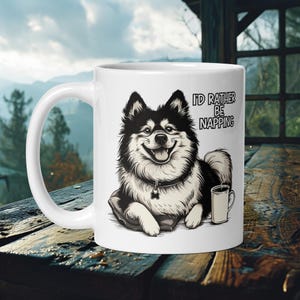 Pode incluir: Caneca de cerâmica branca com uma ilustração em preto e branco de um cão segurando uma xícara de café. O texto "I'd rather be napping" está impresso na caneca.