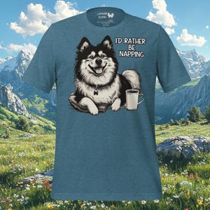 Pode incluir: Uma camiseta azul com um cão de desenho animado preto e branco usando uma coleira e uma xícara de café. O texto na camiseta diz "I'd rather be napping".