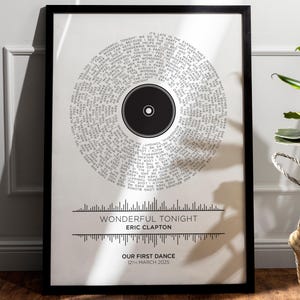 May include: A black and white printable art print featuring the lyrics to the song "Wonderful Tonight" by Eric Clapton. The lyrics are arranged in a circle around a black record. The text "Our First Dance" and the date "12th March 2025" are printed below the lyrics.