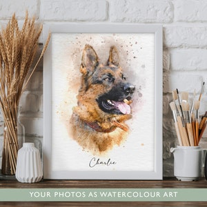 May include: A framed watercolour portrait of a German Shepherd dog with brown and black fur, featuring a pink tongue and a brown collar. The name Charlie is printed in black script below the dog. The artwork is displayed in a white frame.