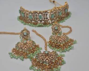 May include: A gold-toned jewelry set featuring a choker necklace, earrings, and a headpiece. The set is adorned with light green and peach-colored beads and gemstones. The intricate design showcases a blend of elegance and detail, perfect for special occasions.