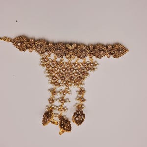 May include: A gold-tone necklace with a delicate chain and a pendant featuring a floral design with clear and white stones. The pendant is attached to a long chain with multiple strands of pearls and smaller floral accents.