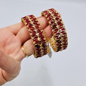 May include: Two gold bangles set with red and white stones. The bangles are stacked on top of each other.