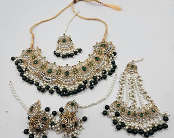 Op de afbeelding: Een goudkleurige sieradenset met een ketting, oorbellen en een hoofdband. De ketting en hoofdband hebben een bloemmotief met heldere en groene edelstenen en zwarte kraalaccenten. De oorbellen zijn rond met vergelijkbare details. Ideaal voor speciale gelegenheden.