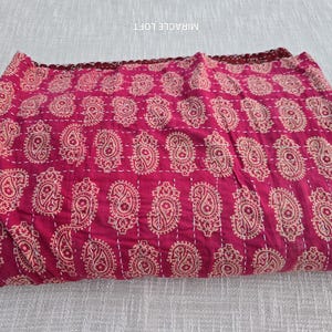 Puede incluir: Una colcha kantha roja con un patrón de paisley. La colcha está doblada y tiene un borde blanco.