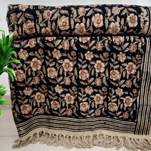 May include: A black floral patterned textile, possibly a throw blanket or rug, with a repeating design of beige flowers and leaves. The edges feature black and white stripes and a fringe. The textile is folded and stacked.