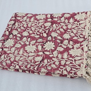 Könnte beinhalten: Gefaltete bordeauxfarbene Wurfadecke mit cremefarbenem Blumenmuster. Die Decke hat einen cremefarbenen Fransenrand. Das florale Design zeigt große Blumen und Blätter. Diese dekorative Decke ist für ein Bett oder Sofa geeignet.