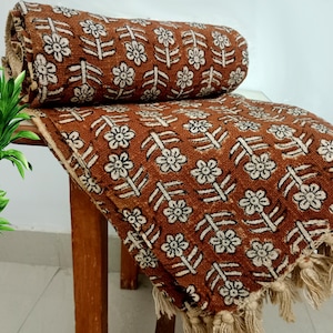 May include: A brown and white patterned throw blanket with fringe. The blanket is folded and draped over a wooden chair.